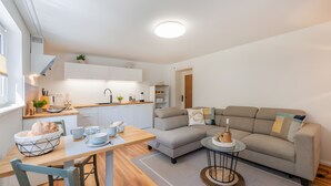 Una cocina moderna con armarios blancos, una mesa de comedor con sillas y una sala de estar con sofá y mesa baja.