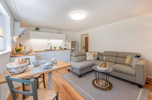 Eine moderne Küche mit weißen Schränken, einem Esstisch mit Stühlen und einer Wohnbereits mit einer Couch und Couchtisch.