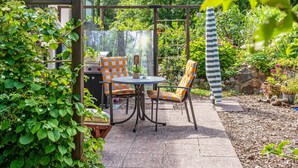 Un patio al aire libre con una mesa y sillas, rodeado de abundante vegetación y un muro de piedra.