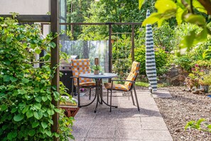Eine Terrasse im Freien mit Tisch und Stühlen, umgeben von üppiger Bepflanzung und einer Steinmauer.