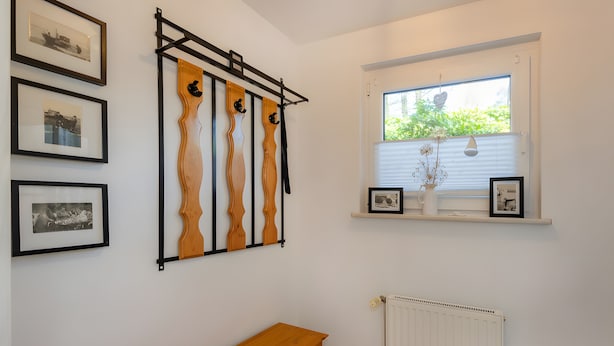 Una habitación con un banco de madera, un radiador, una ventana con persianas y cuadros enmarcados en la pared.