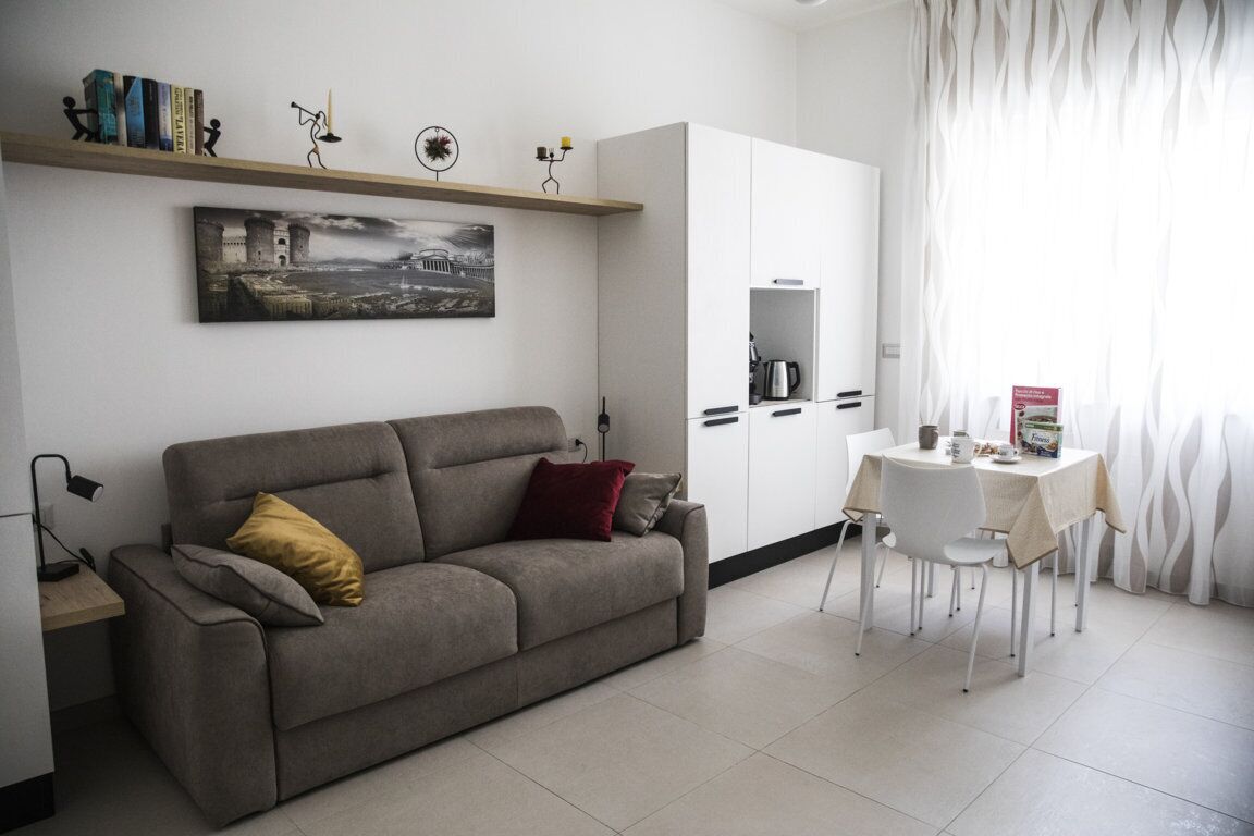 A modern living room with a sofa, a dining table with chairs, a bookshelf, and a painting on the wall.