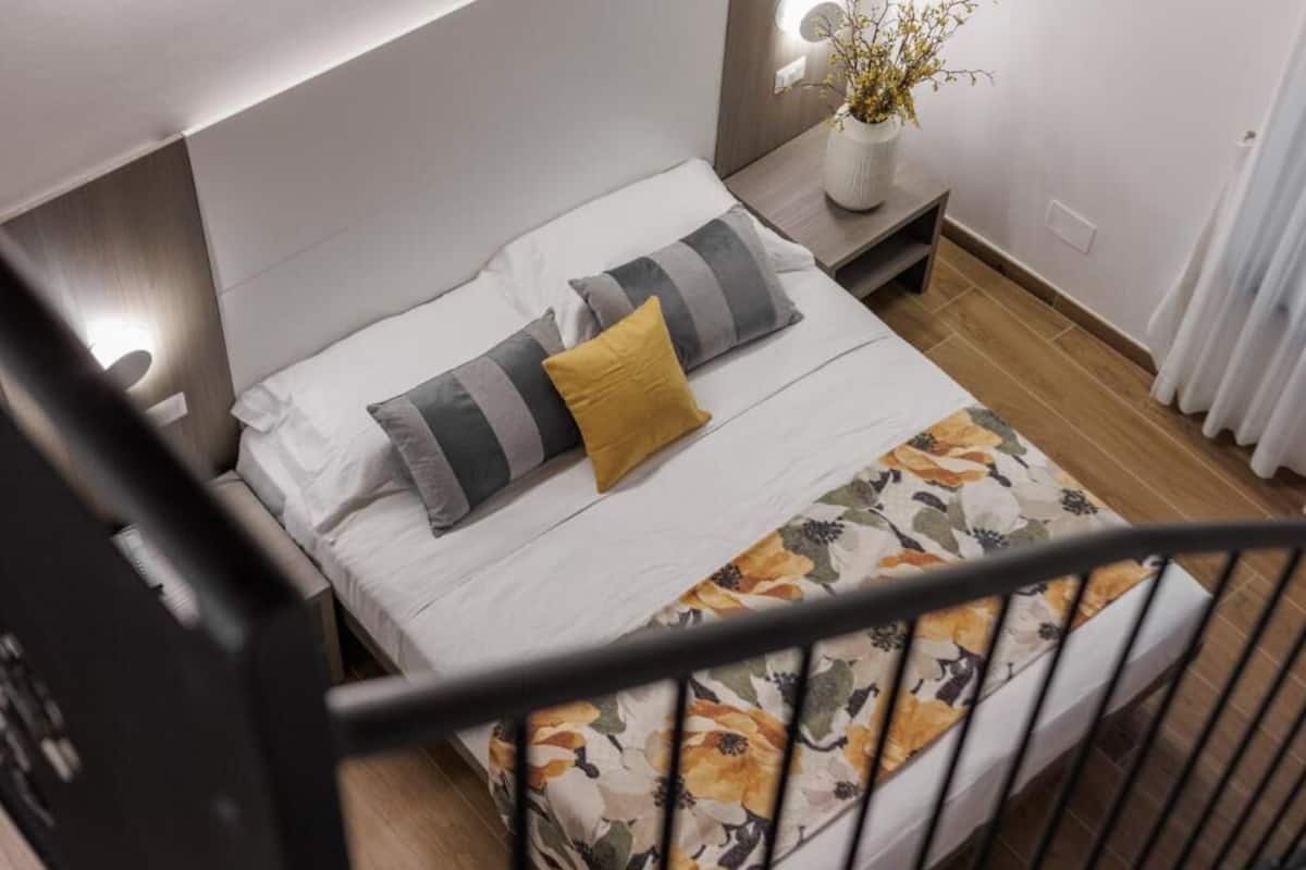 Une chambre à coucher avec un lit, des oreillers, une table de chevet et un vase rempli de fleurs.