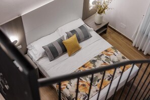 Una camera da letto con un letto, cuscini, un comodino e un vaso con fiori.