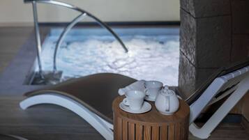 Un área de spa con una mesita de madera que sostiene tazas y un calentador de agua, una silla de lounge y una bañera de hidromasaje con un grifo metálico.