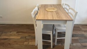 A dining table with a woven placemat, surrounded by white chairs, in a room with wooden flooring and a plain wall. - Cosy F2 separate sleeping area on ground floor in quiet pedestrian alley close to all amenities (Orléans)