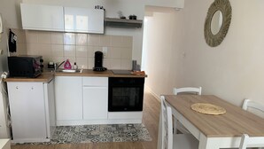 A compact kitchen with white cabinets, a built-in oven, a coffee maker, and a dining area with a wooden table and chairs. - Cosy F2 separate sleeping area on ground floor in quiet pedestrian alley close to all amenities (Orléans)