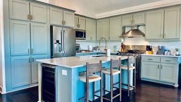 A spacious kitchen with light blue cabinets, a central island with bar stools, stainless steel appliances, and a dark wood floor.