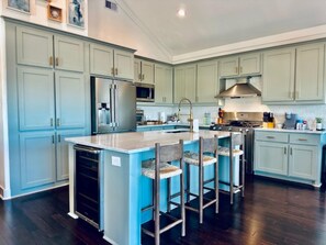 Una cocina amplia con armarios azul claro, una isla central con taburetes de bar, electrodomésticos de acero inoxidable y piso de madera oscura.
