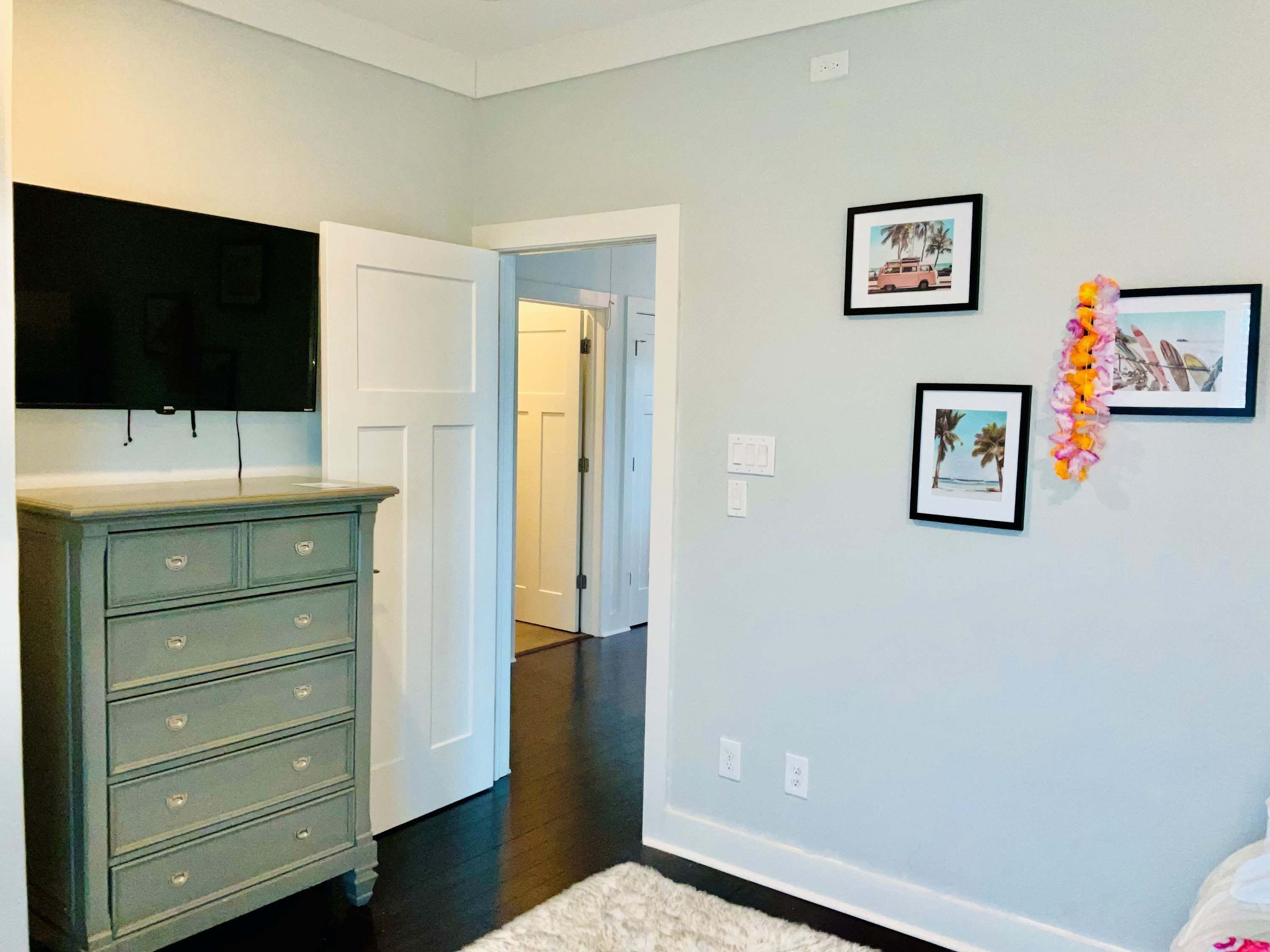 Une chambre à coucher avec une commode, un téléviseur fixé au mur et des tableaux encadrés.
