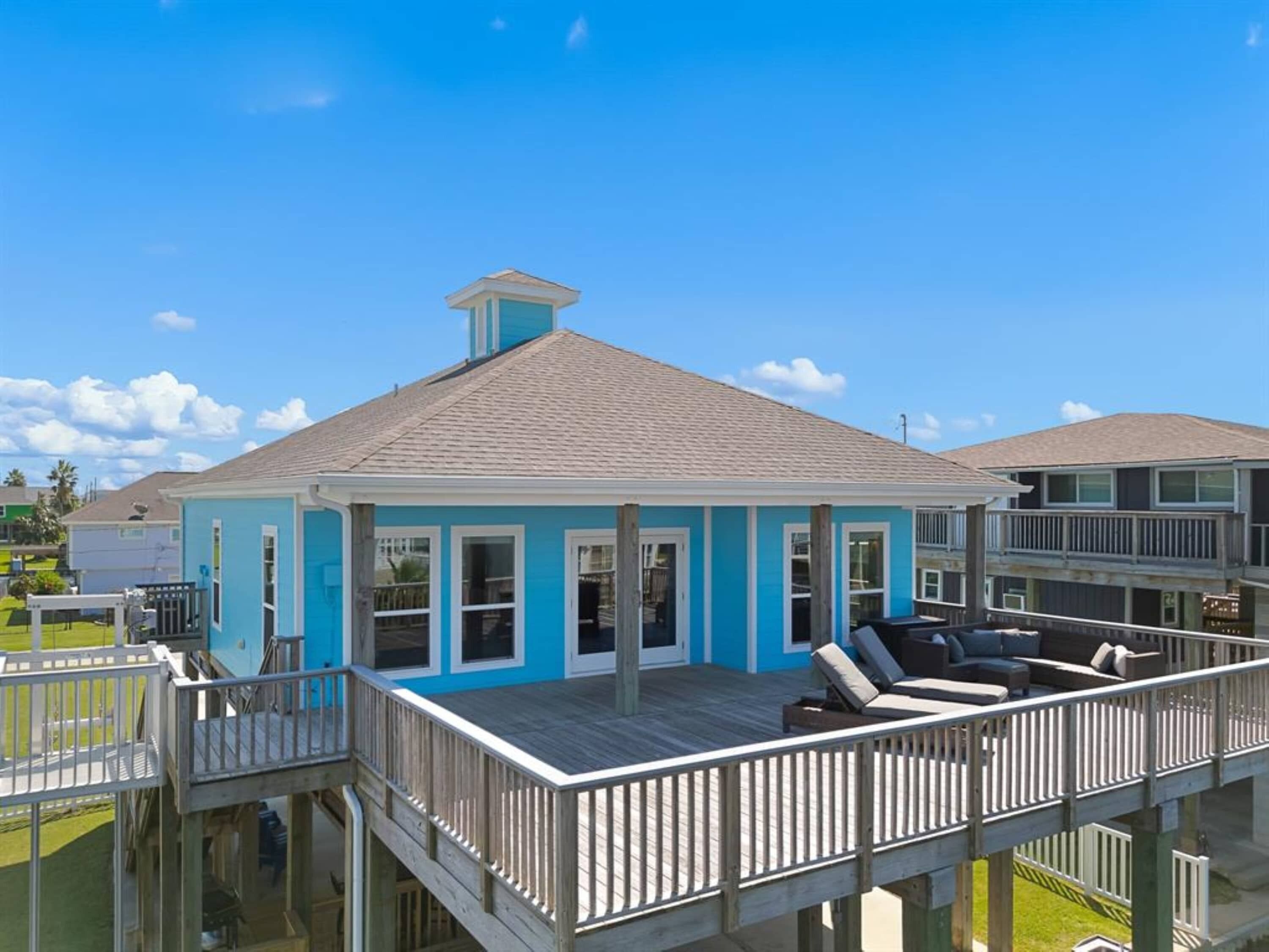 A two-story house with a blue exterior, a wooden deck, and a covered outdoor seating area.