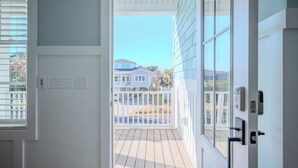 Une vue depuis une porte donnant sur un balcon, avec un ciel dégagé, une balustrade blanche et un bâtiment en arrière-plan.