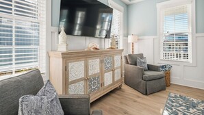 Un salon avec un canapé gris, un fauteuil gris, un meuble en bois orné de motifs décoratifs, un téléviseur à écran plat et un tapis à motifs.