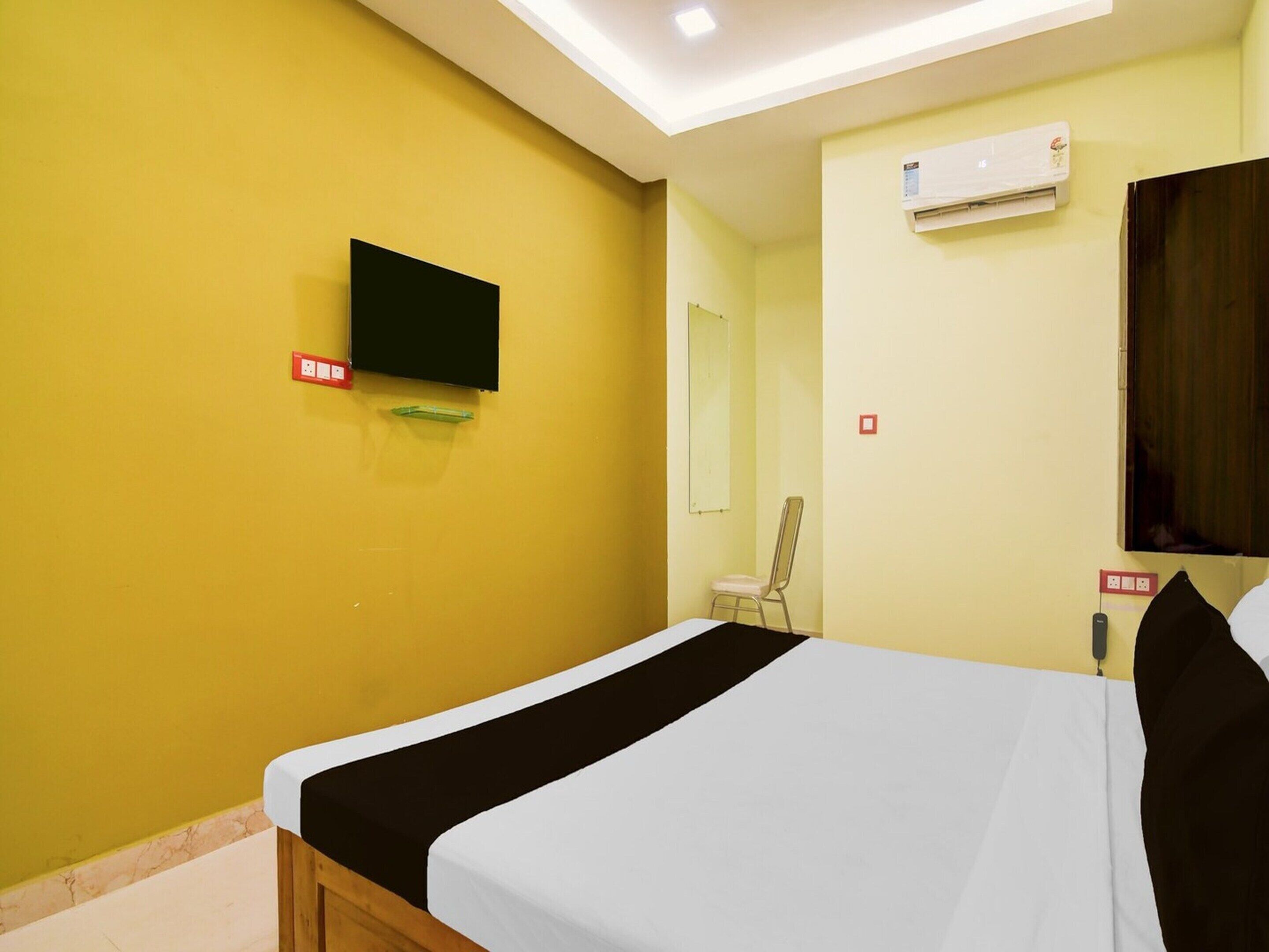 A hotel room with a bed, a television mounted on the wall, an air conditioning unit, and a mirror.