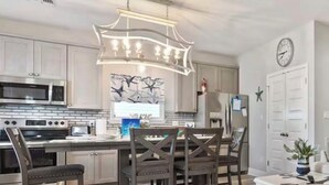 A modern kitchen with stainless steel appliances, a dining area with wooden chairs, and a white table.