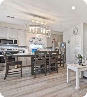 A modern kitchen with stainless steel appliances, a dining area with wooden chairs, and a white table.