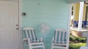A porch with two white wicker chairs with blue and white striped cushions, a small white wicker table, and a white fan.