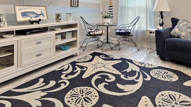 A living room with a flat-screen TV, a dining table with chairs, a sofa, and a decorative rug.