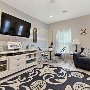Sala de estar com televisão de tela plana, mesa de jantar com cadeiras, sofá e tapete decorativo.