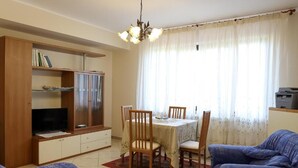 A living room with a dining table, chairs, a television on a cabinet, and a sofa. - Tenuta Albachiara (Naso)