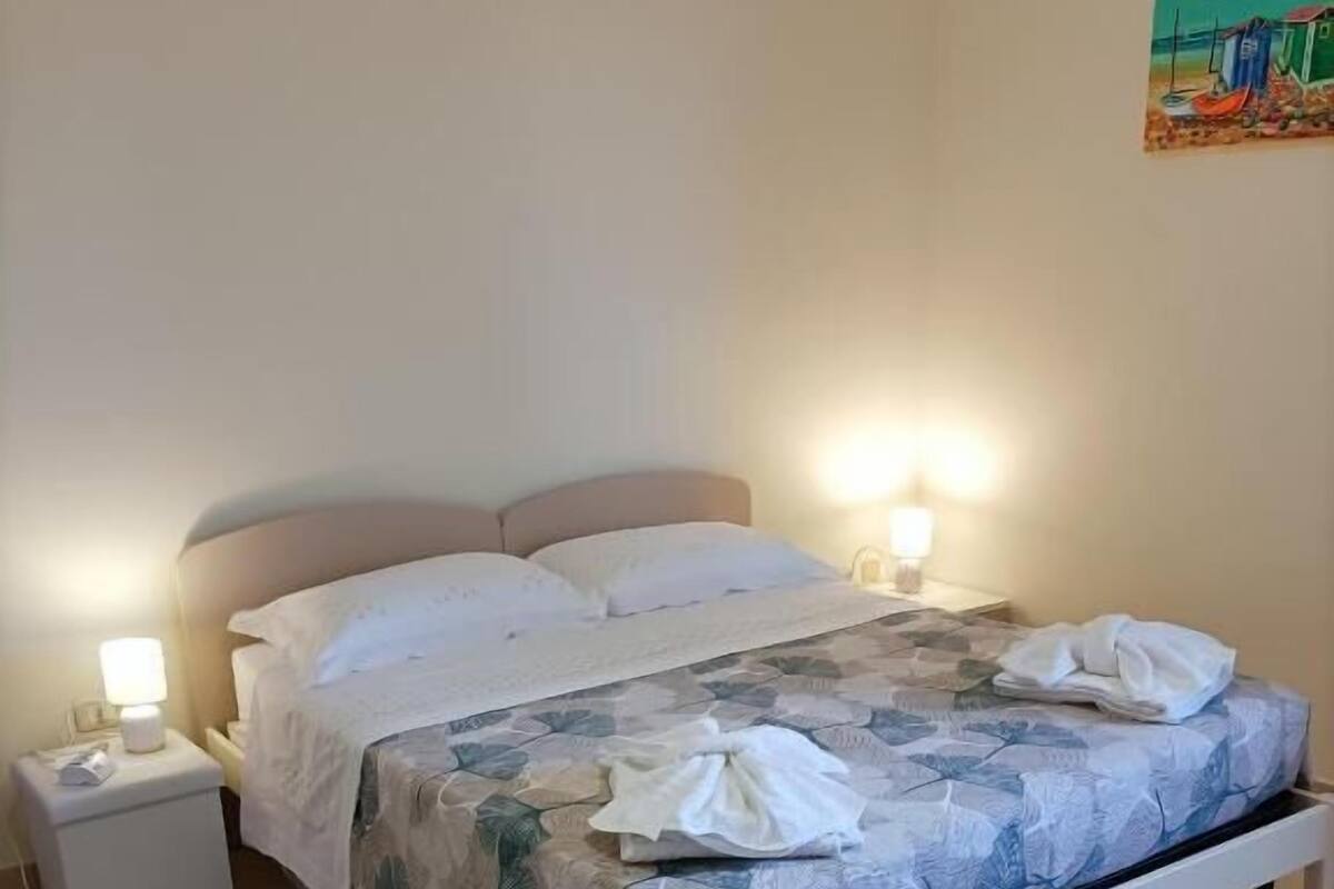 A neatly made bed with a floral bedspread, two bedside lamps, and a small bedside table.