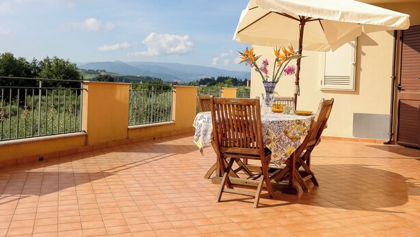 A terrace with a table and chairs, an umbrella, and a vase with flowers. - Tenuta Albachiara (Naso)