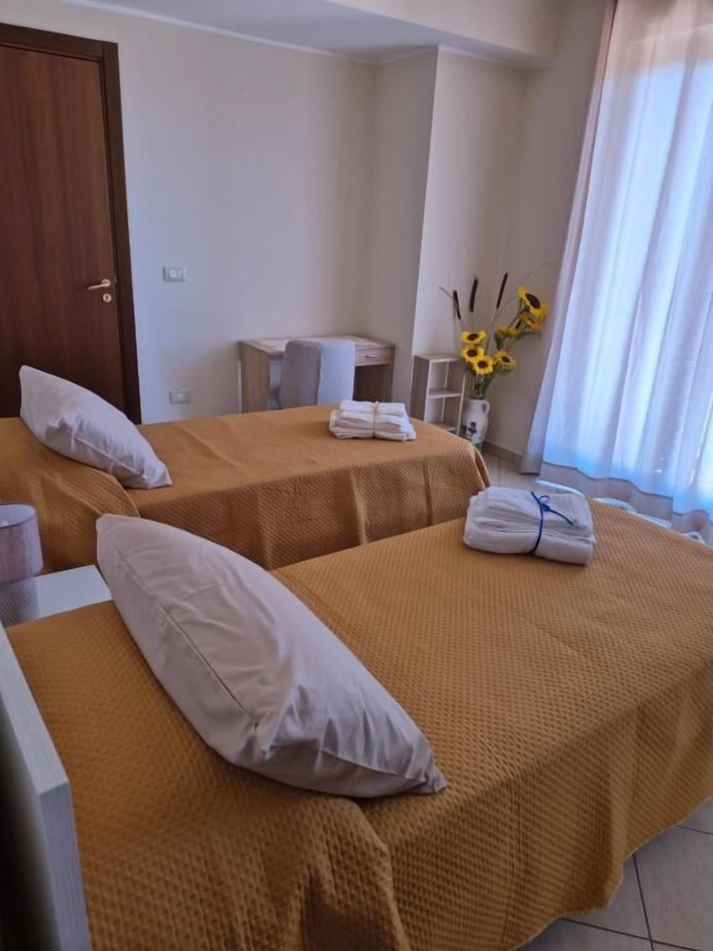 Habitación de hotel con dos camas, un escritorio, una silla y un jarrón con girasoles.