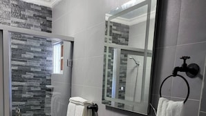 A modern bathroom with a black sink, a mirror, and a shower area with a stone wall. - Modern 1 Bedroom Apt 5B (Puerto Plata)