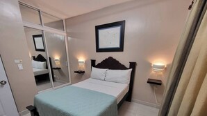 A neatly arranged hotel room with a bed, bedside tables, a wall-mounted picture, and a mirror. - Modern 1 Bedroom Apt 5B (Puerto Plata)