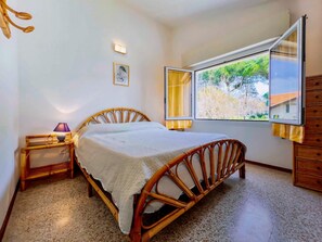Un dormitorio con una cama de madera, una mesita de noche con una lámpara, una ventana con cortinas y un cuadro colgado en la pared.