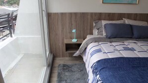 Un dormitorio con cama, mesita de noche, lámpara de pie, ventana y balcón.