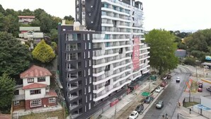 Un edificio de varios pisos con balcones, un estacionamiento y una carretera con vehículos.