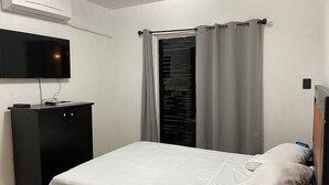 A bedroom with a bed, a TV mounted on the wall, a wardrobe, and a window with curtains.