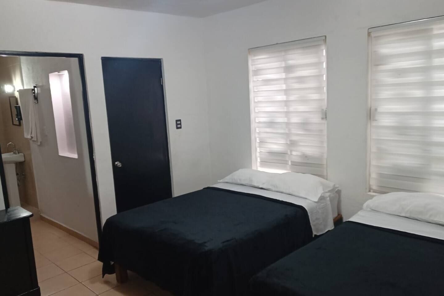 Quarto com duas camas, uma porta, uma janela e uma pia.