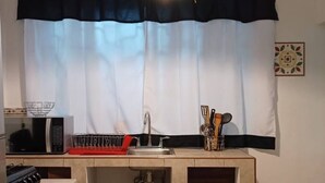 A compact kitchen with a microwave, sink, and utensil holder.