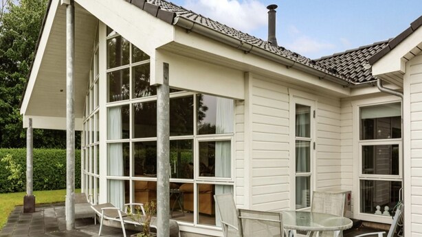 Un patio cubierto con mesa y sillas, ventanas grandes y una chimenea.