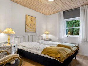 Une chambre à coucher comprenant un lit, deux tables de chevet avec des lampes, une fenêtre avec des rideaux et une œuvre d’art accrochée au mur.