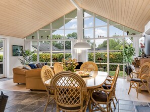 Une pièce spacieuse avec un plafond haut, de grandes fenêtres, une table à manger avec des chaises, un canapé et un téléviseur.