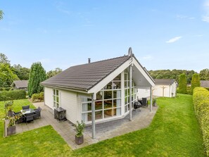 A modern house with a sloped roof, large windows, and a patio with outdoor furniture.