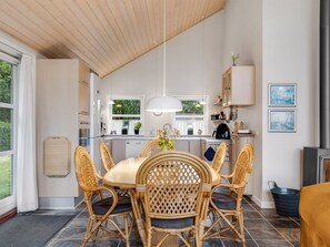 Une cuisine moderne avec un coin repas, comprenant une table ronde, des chaises en osier et un luminaire suspendu.