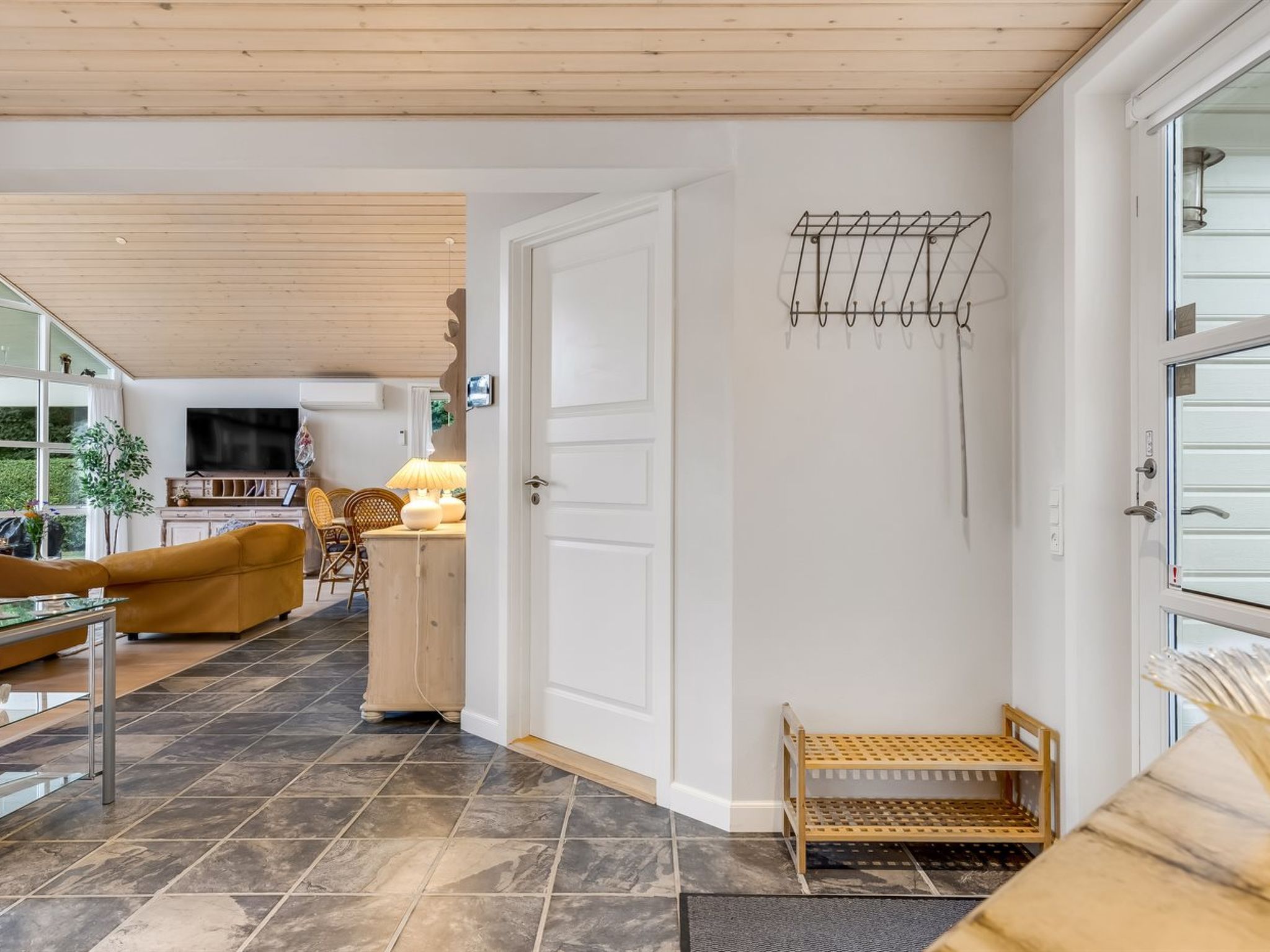 Un interior moderno con techo de madera, un televisor, un sofá, una zona de comedor y una puerta con perchero.