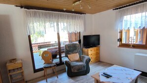 Una sala de estar acogedora con techo de madera, un televisor, un sofá, un sillón y una mesita con mandos a distancia.