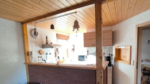 Una cocina rústica con vigas de madera, una isla de ladrillo y utensilios de cocina colgando.