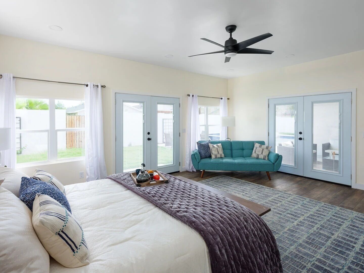 A bedroom with a bed, a teal sofa, and a ceiling fan.