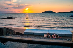 Une vue sur la plage avec un coucher de soleil, une piscine et une petite île au loin.