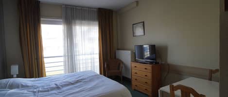 Una habitación de hotel con cama, escritorio, silla, televisor y ventana con cortinas.