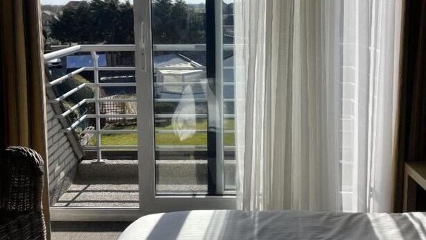 Een hotelkamer met een groot bed, uitzicht op een balkon en een schuifdeur.