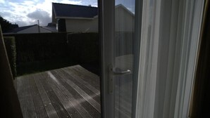 Een houten terras met een glazen deur naar een achtertuin.