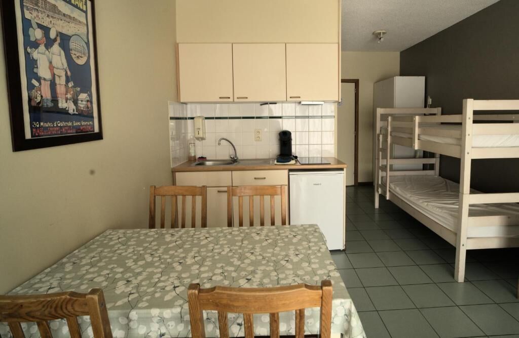 Een kleine kamer met een eettafel, een kitchenette en een stapelbed.