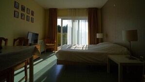 Een hotelkamer met een bed, een bureau, een stoel, een televisietoestel en een raam met gordijnen.